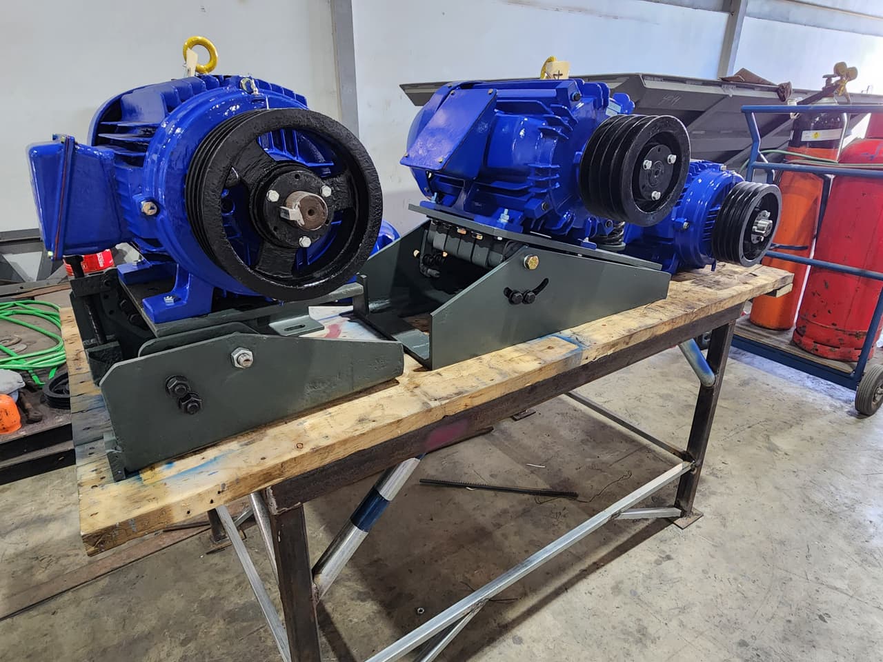 Two blue electric motors with belt pulleys on a mounting base in the workshop