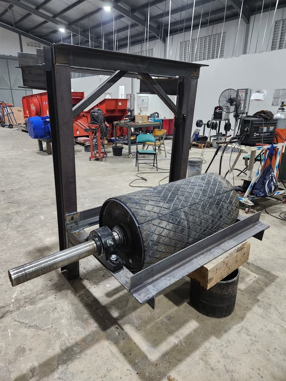 Rubber-lagged conveyor drive pulley with shaft and bearings on a workshop stand